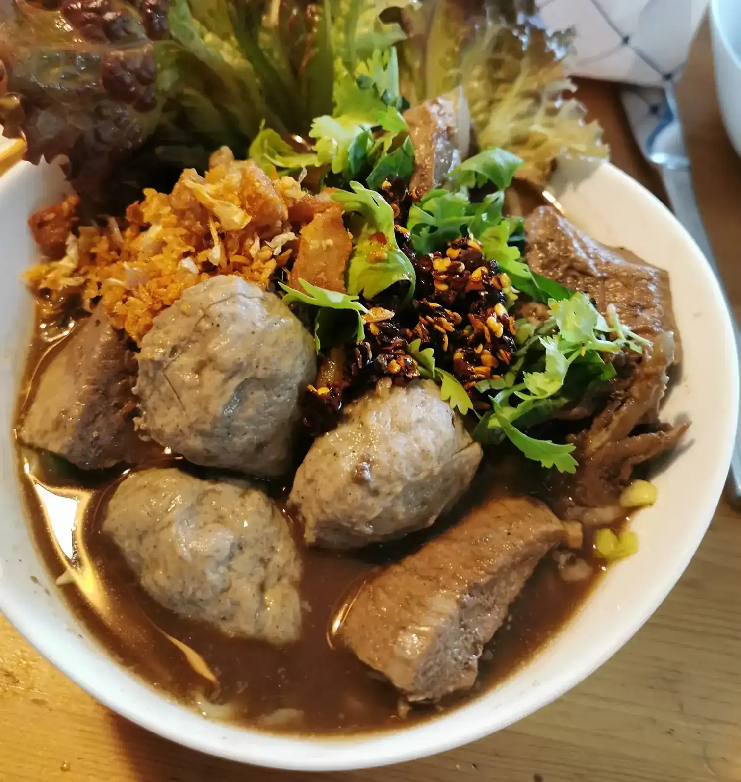 A bowl of braised noodle soup with meatballs, coriander, roasted chilli and fried garlic