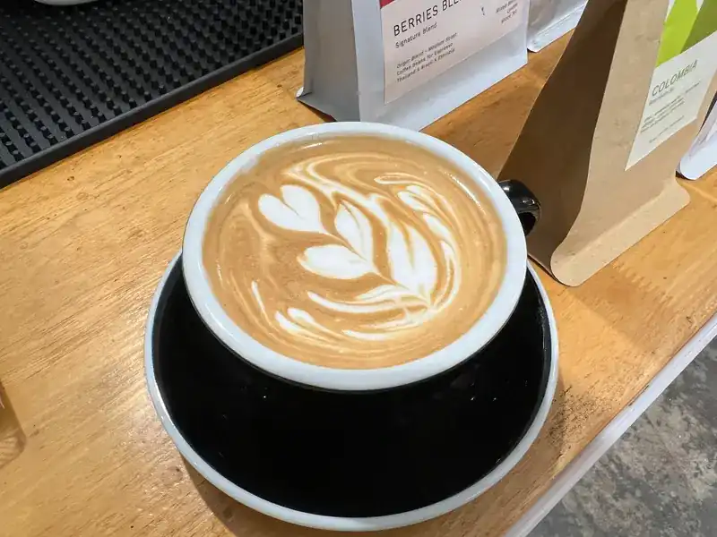 A cappuccino with latte art on the wooden bar, bags of coffee beans behind it