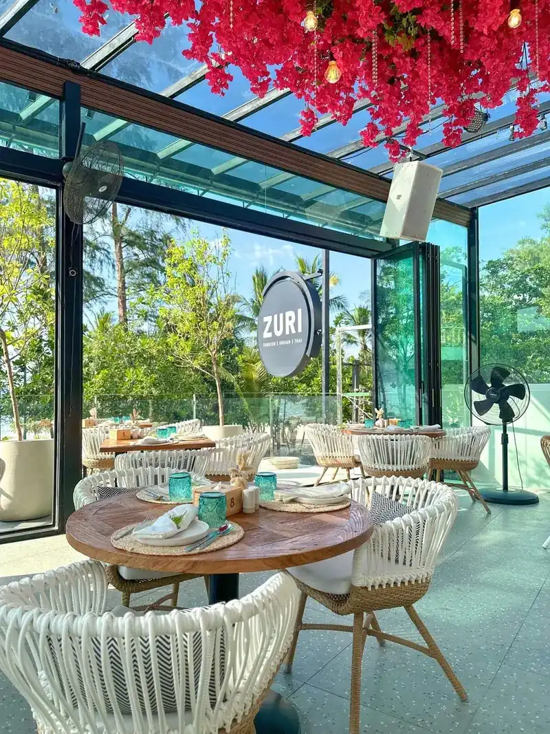 Round table by the glass wall with palm trees and the Zuri sign outside
