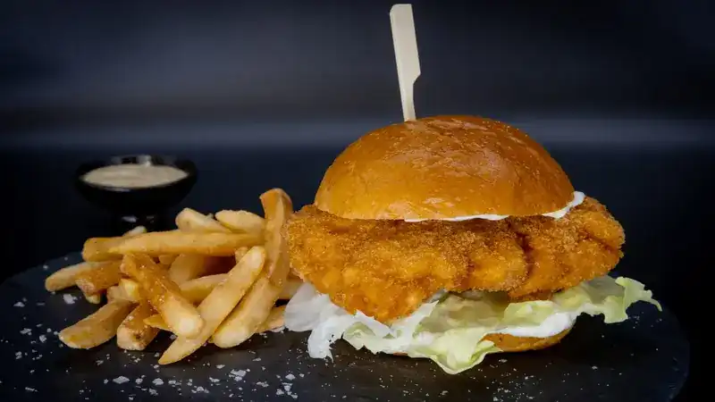 A crisp burger with lettuce, fries and a dip on a slate
