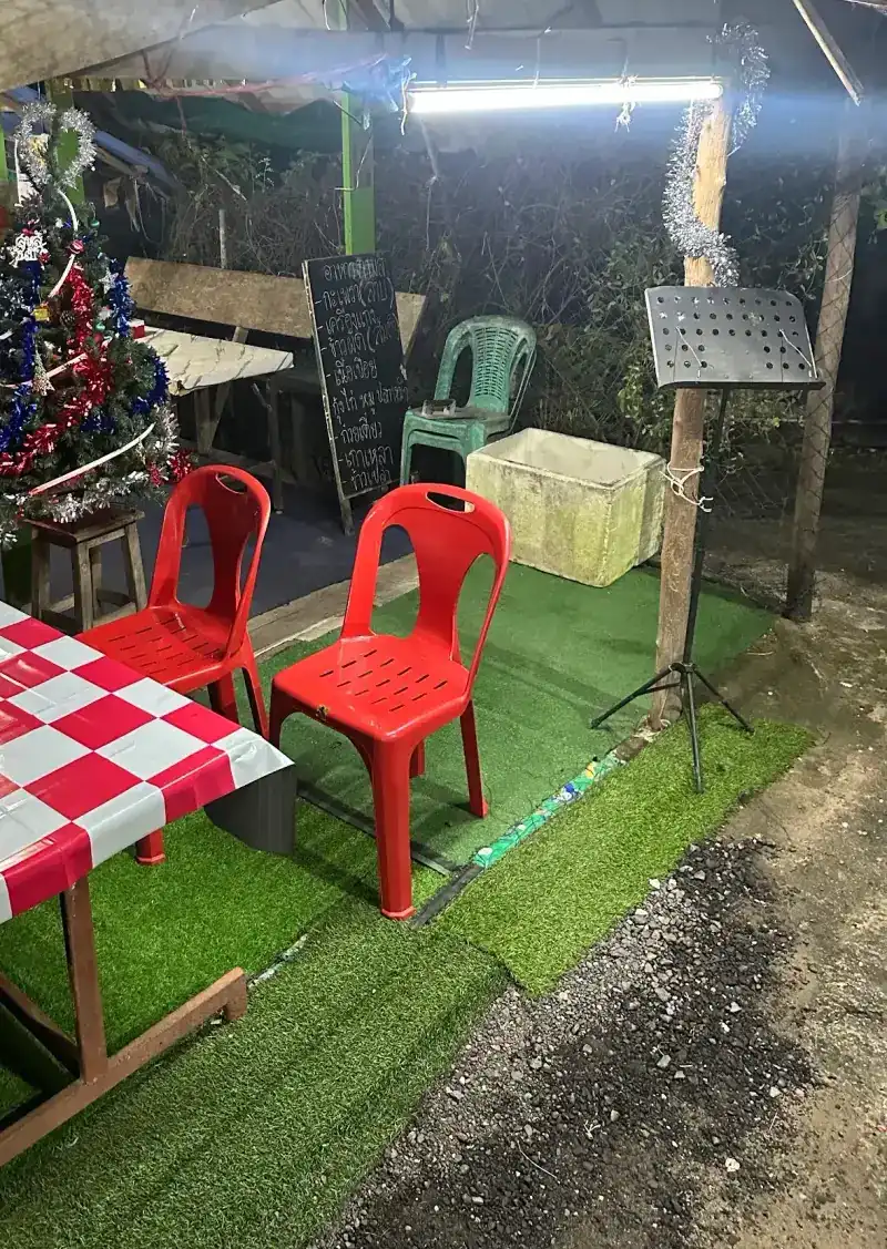 The open-sided shelter at night: a table with red-and-white checked oilcloth, red plastic chairs on artificial grass and a handwritten chalkboard