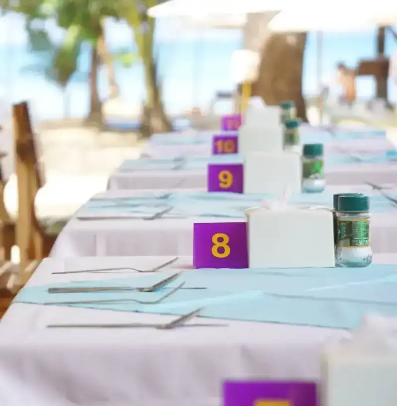 A row of tables with purple table-number cards, the beach behind
