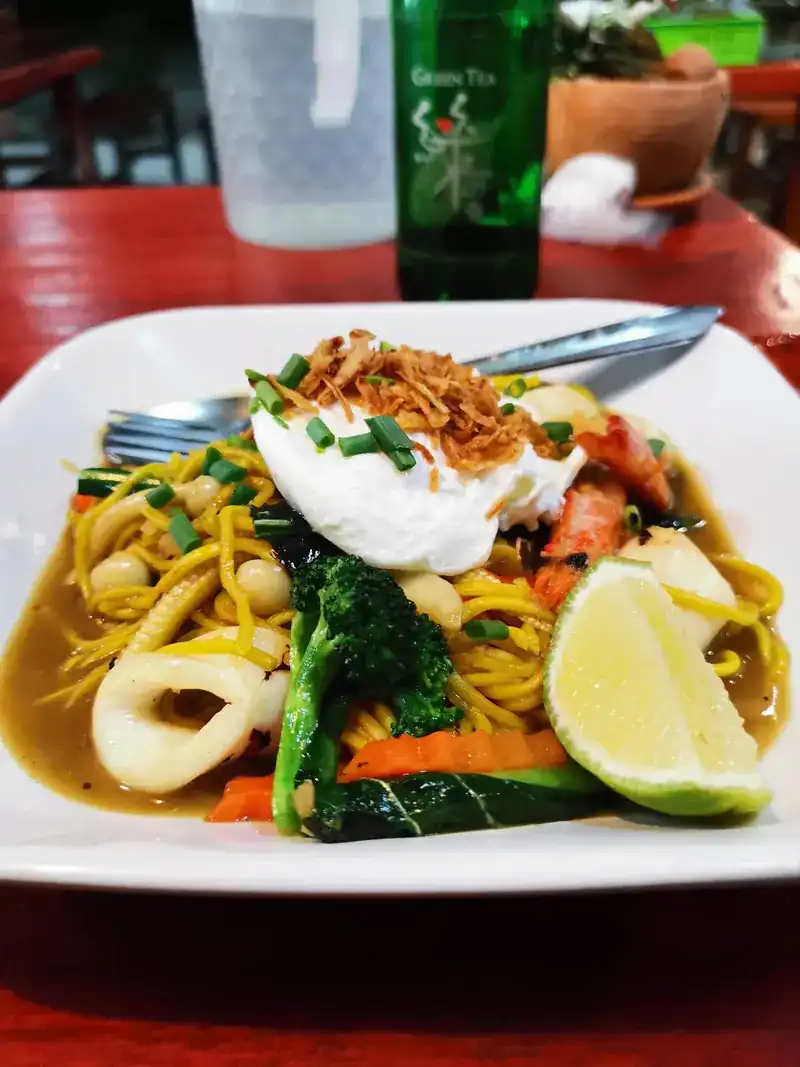 Yellow noodles with a poached egg, squid, prawn and broccoli, topped with fried shallots