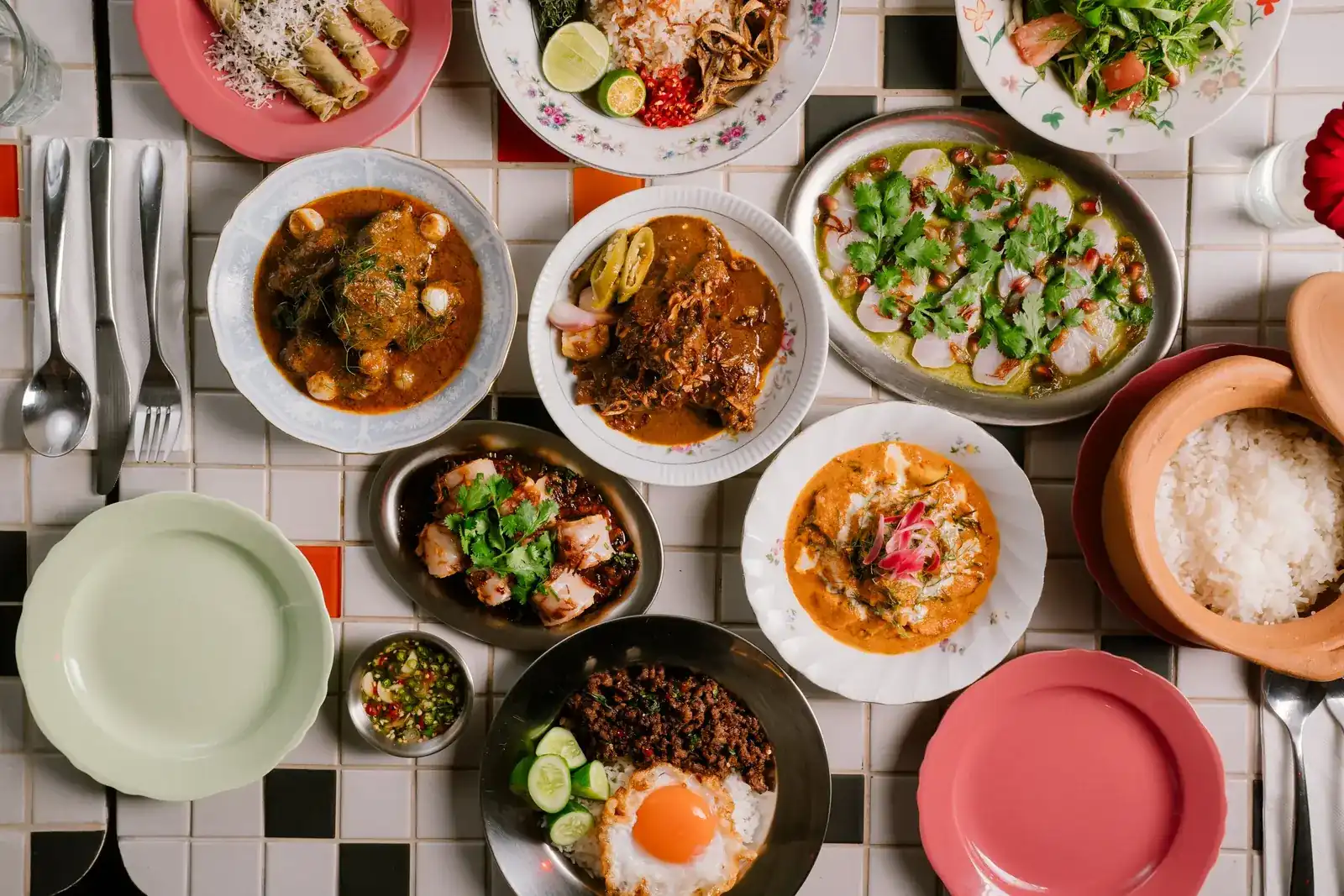 Curries, stir-fries, a fried egg and a clay pot of rice laid out on a black and white tile table