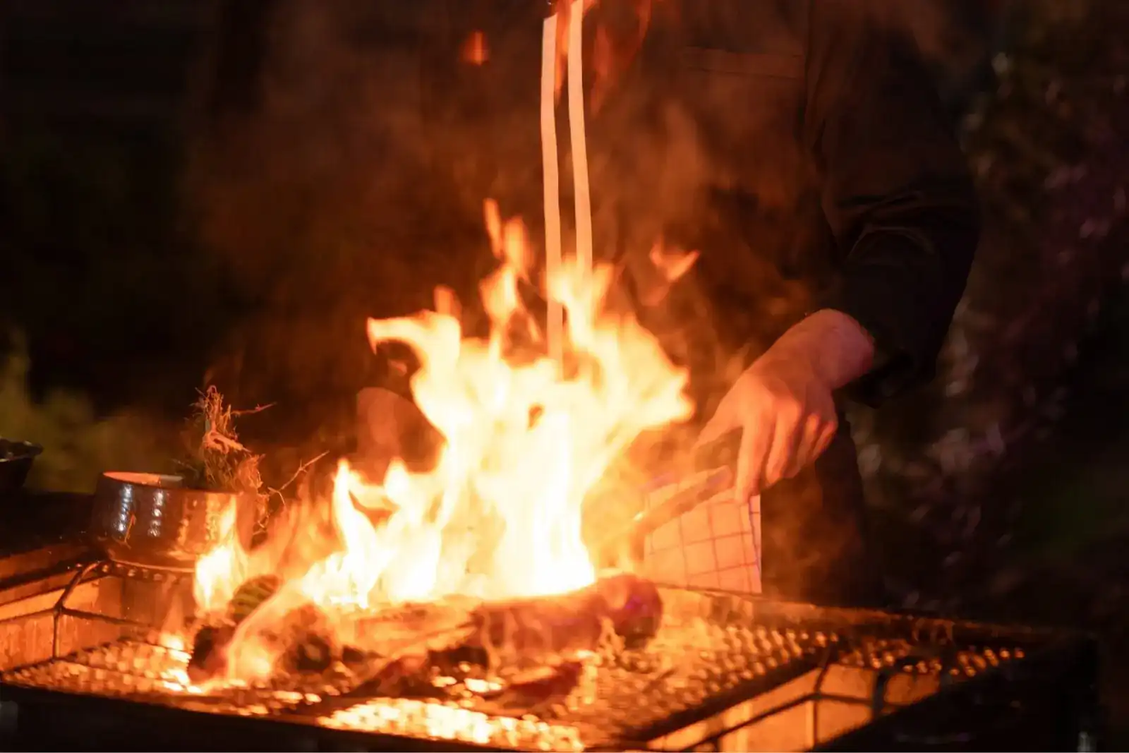 Flames rising from the charcoal grill as a cook turns the meat