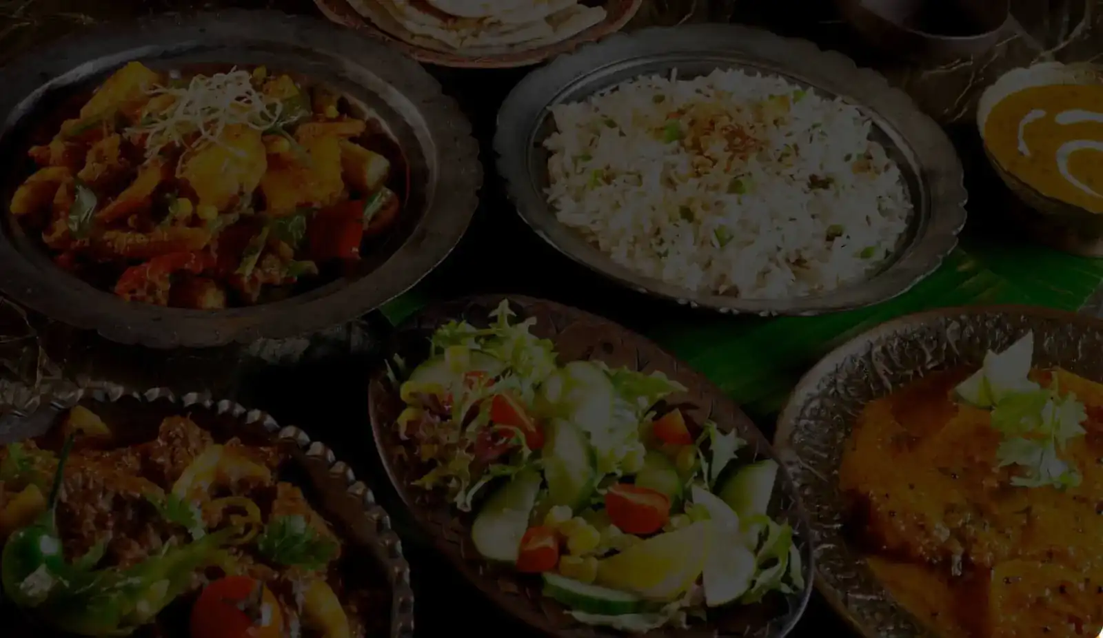 Engraved metal dishes of curry, rice with peas and fresh salad on a banana leaf