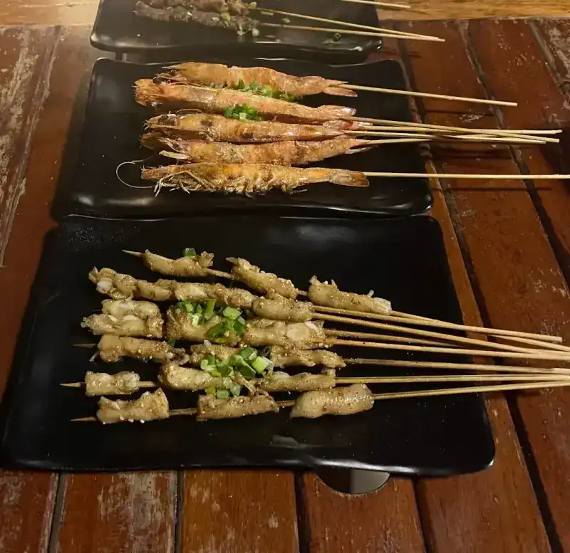 Grilled prawns and other skewers on black plates