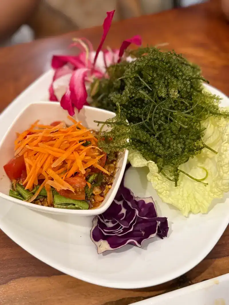 Sea grapes next to a salad of shredded carrot, long beans and tomato, with a pink flower