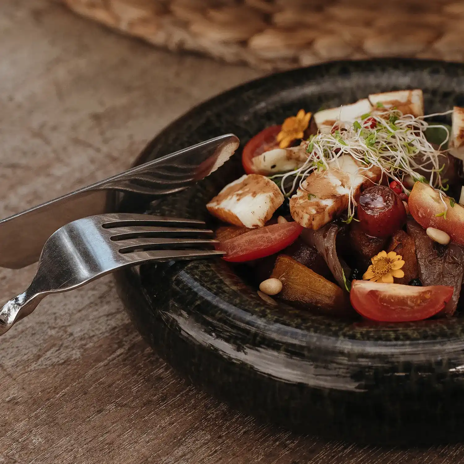 Grilled halloumi, roast pumpkin and cherry tomatoes in a dark stoneware bowl