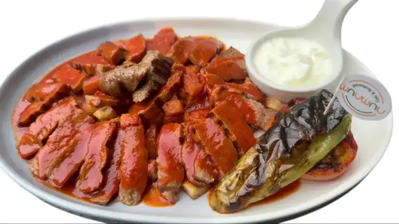 Sliced grilled meat in tomato sauce with yoghurt and a charred green pepper