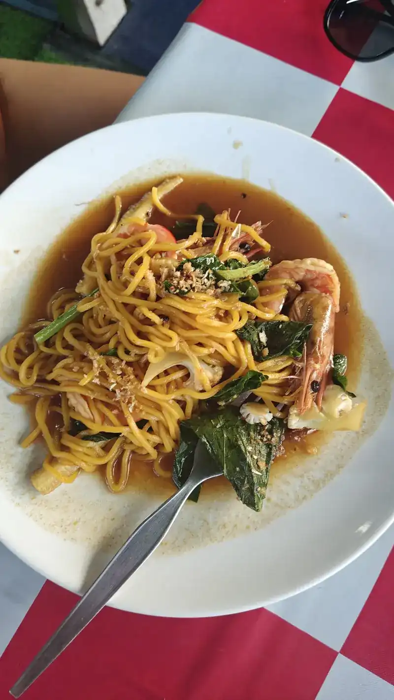 Yellow noodles fried with prawns and green leaves