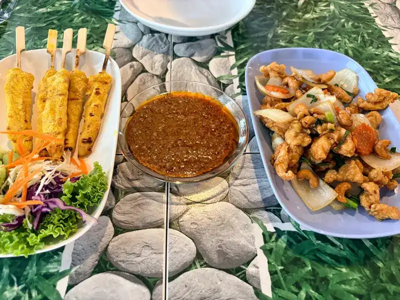 Satay skewers with a bowl of peanut sauce, and a stir-fry with onion