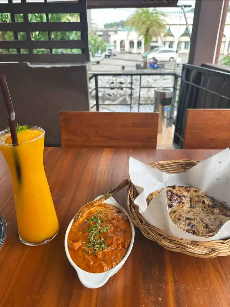 A tall orange drink, a curry and naan on a table above the street