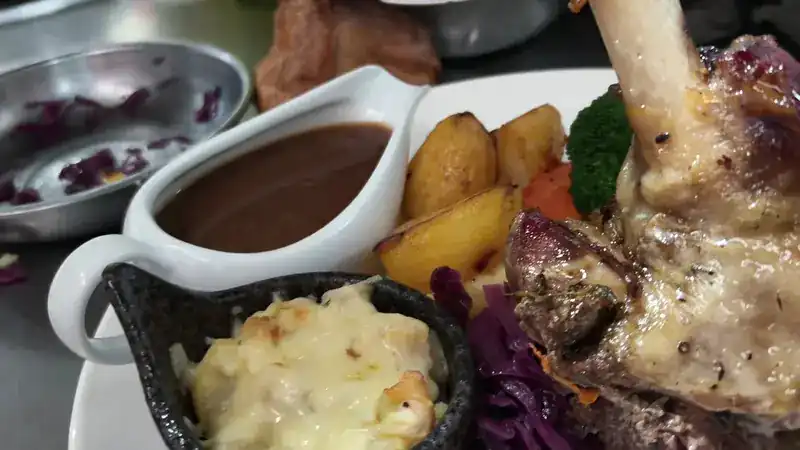 Lamb shank with roast potatoes, red cabbage, cauliflower cheese and a jug of gravy