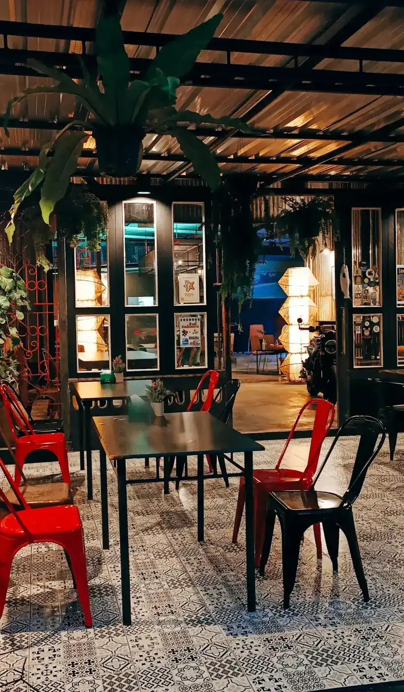 Red metal chairs at black tables on black-and-white patterned floor tiles, with ferns hanging from the beams