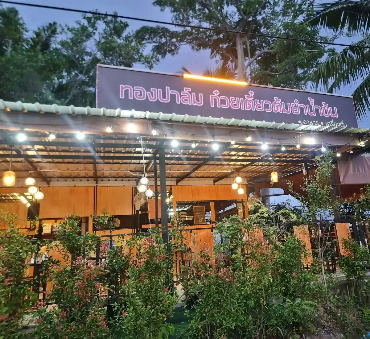 Thongpalm's lit sign above the open-air restaurant at dusk, among palms and shrubs
