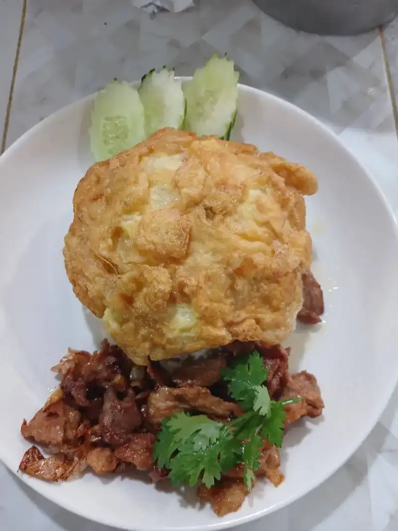 A golden fried egg over stir-fried pork, with cucumber and coriander