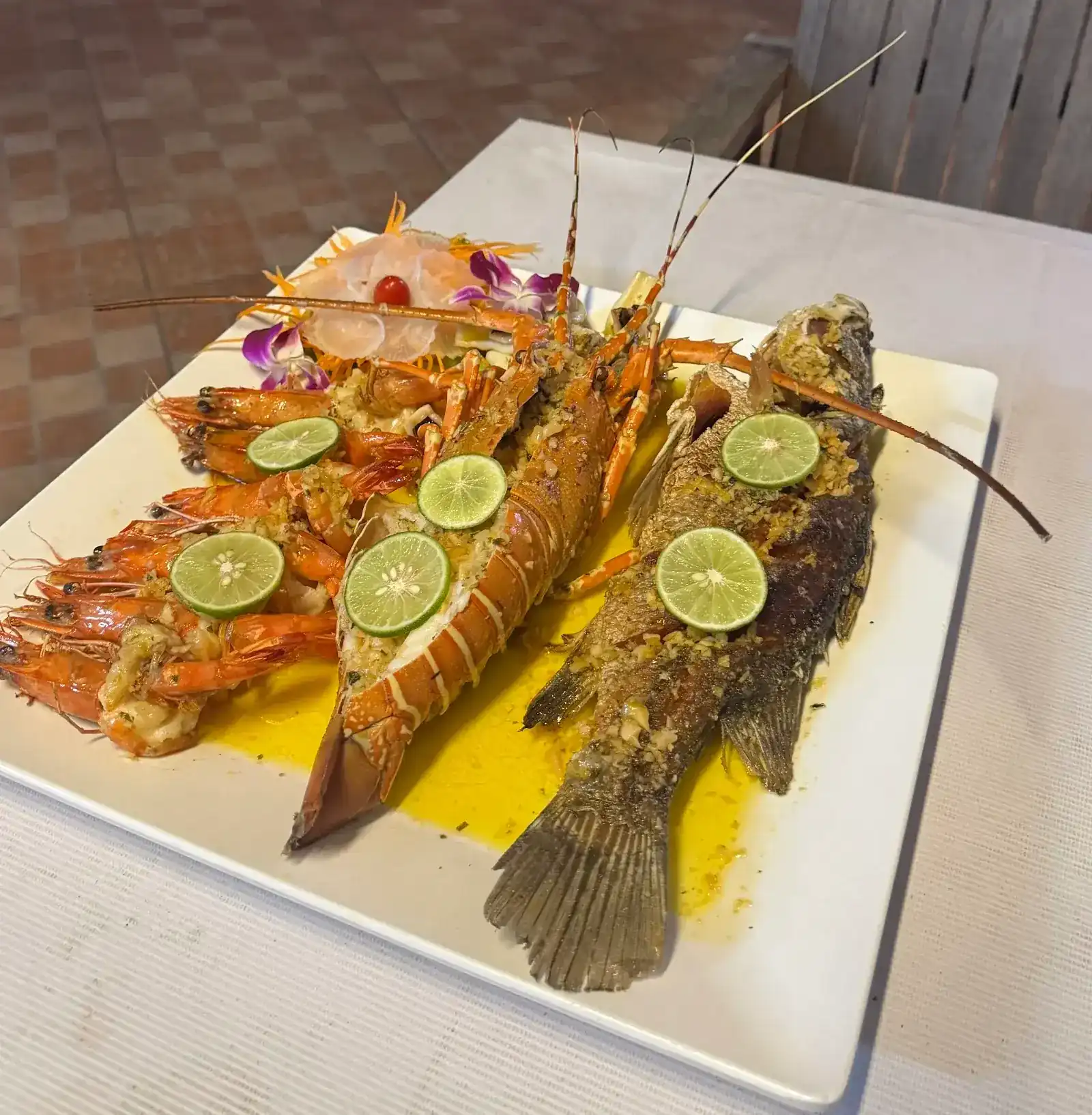 Grilled lobster, prawns and a whole fish with garlic and slices of lime on a white platter