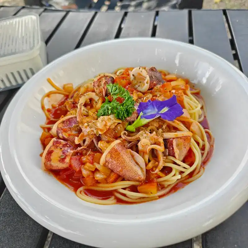 Spaghetti with squid and seafood in tomato sauce, topped with parsley and a butterfly pea flower
