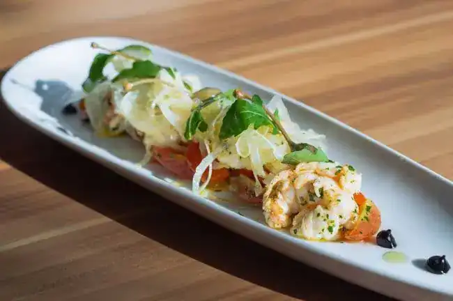 Prawns with shaved fennel, tomato and herbs on a long white plate