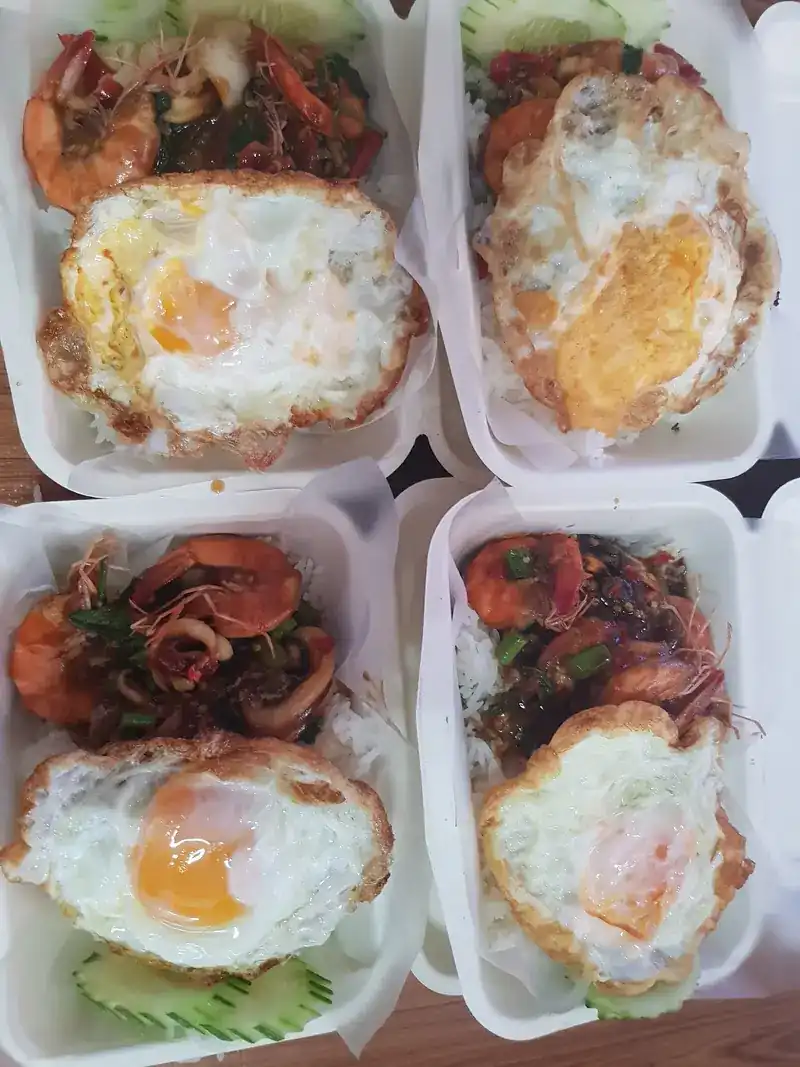 Four takeaway boxes of rice with stir-fried prawns and squid, each with a fried egg