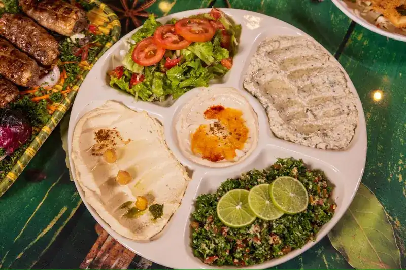 A divided platter of dips, green salad and parsley salad with lime