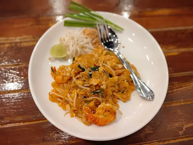 Pad thai with prawns, bean sprouts, lime and chives on a white plate
