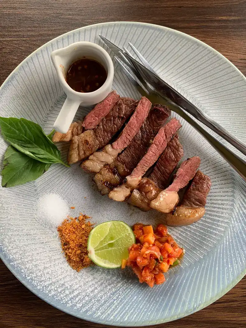 Sliced steak, pink inside, with a dipping sauce, lime and condiments