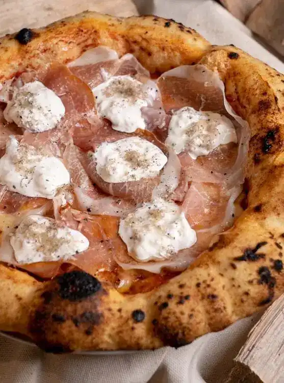Close view of a pizza with a tall, blistered crust, prosciutto and stracciatella