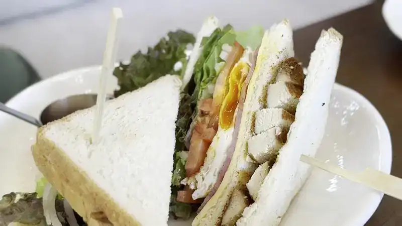 A toasted club sandwich with egg, tomato and salad