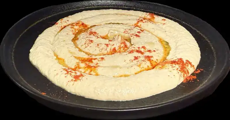 Hummus swirled on a black plate with olive oil and red pepper