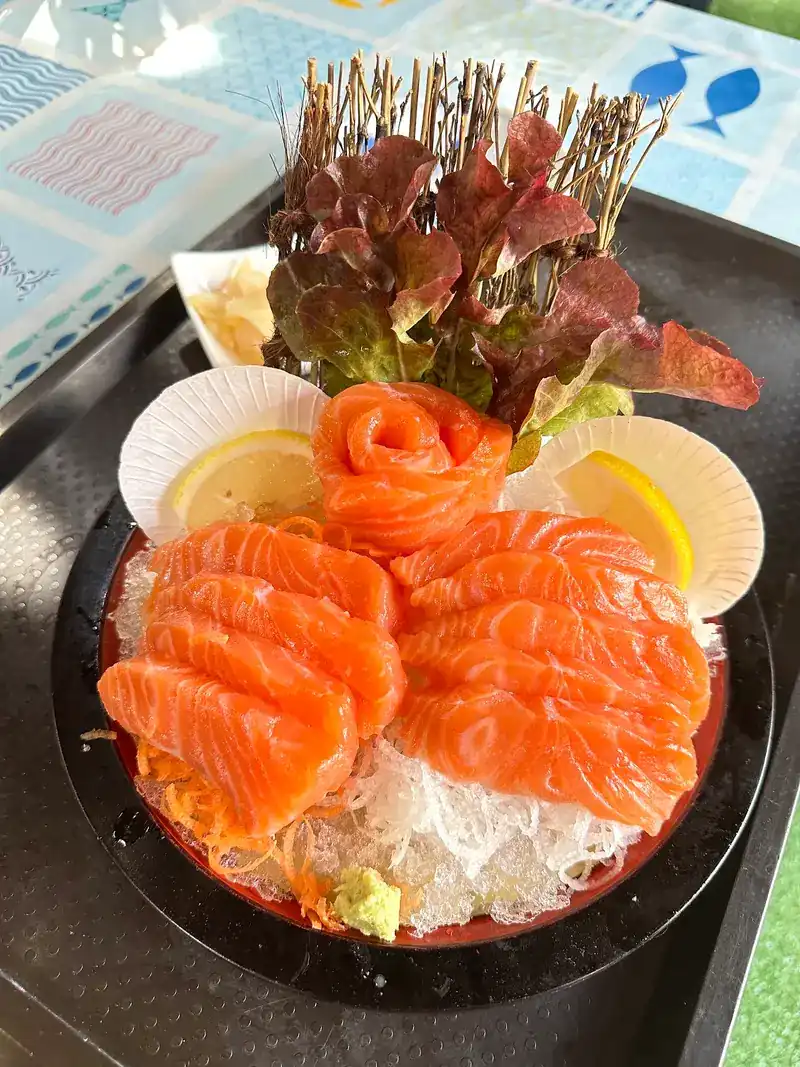 A bowl of salmon sashimi on ice with lemon and lettuce