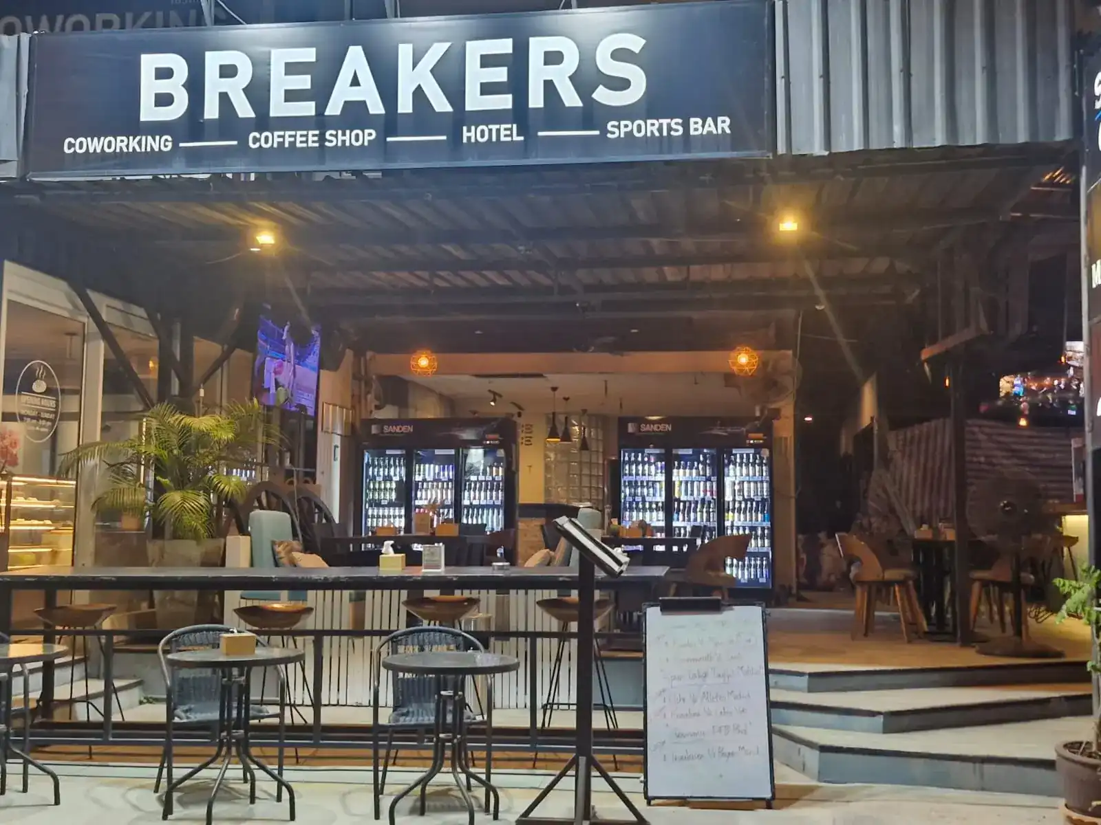 The Breakers front at night: the lit sign, an open terrace with high tables and a screen showing sport