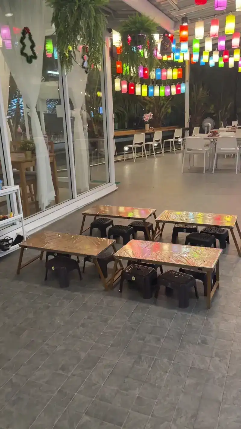 Wooden tables and low stools in a room hung with coloured paper lanterns, at night.