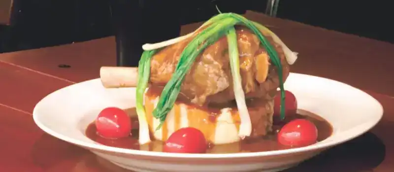 A lamb shank on mashed potato with gravy, spring onions and cherry tomatoes