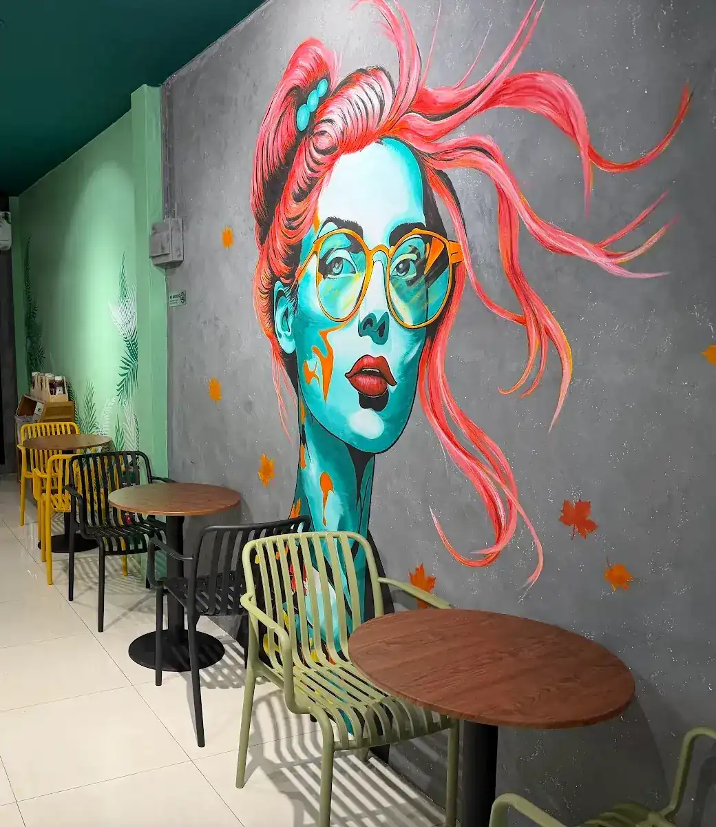 The mural inside Pupa Cafe: a pink-haired girl in yellow glasses above small wooden tables and coloured chairs