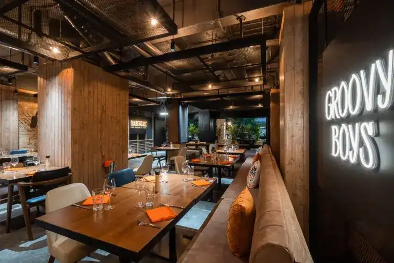 The dining room: timber pillars, a long leather banquette, orange napkins under a steel ceiling