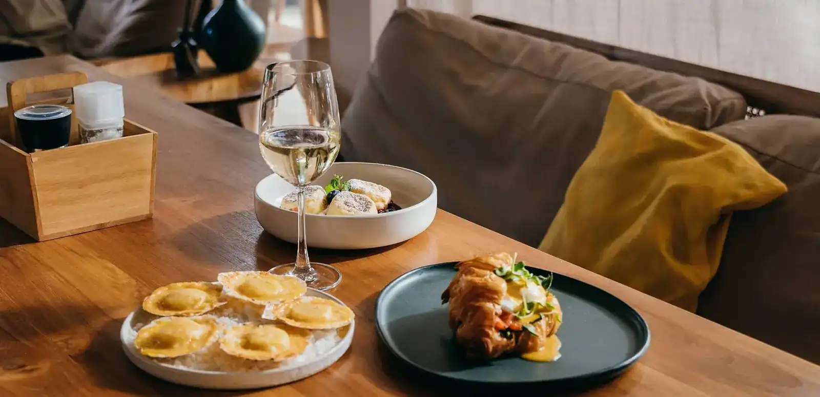 A table at AVO by the sofa: ravioli, a filled croissant, a small bowl and a glass of white wine