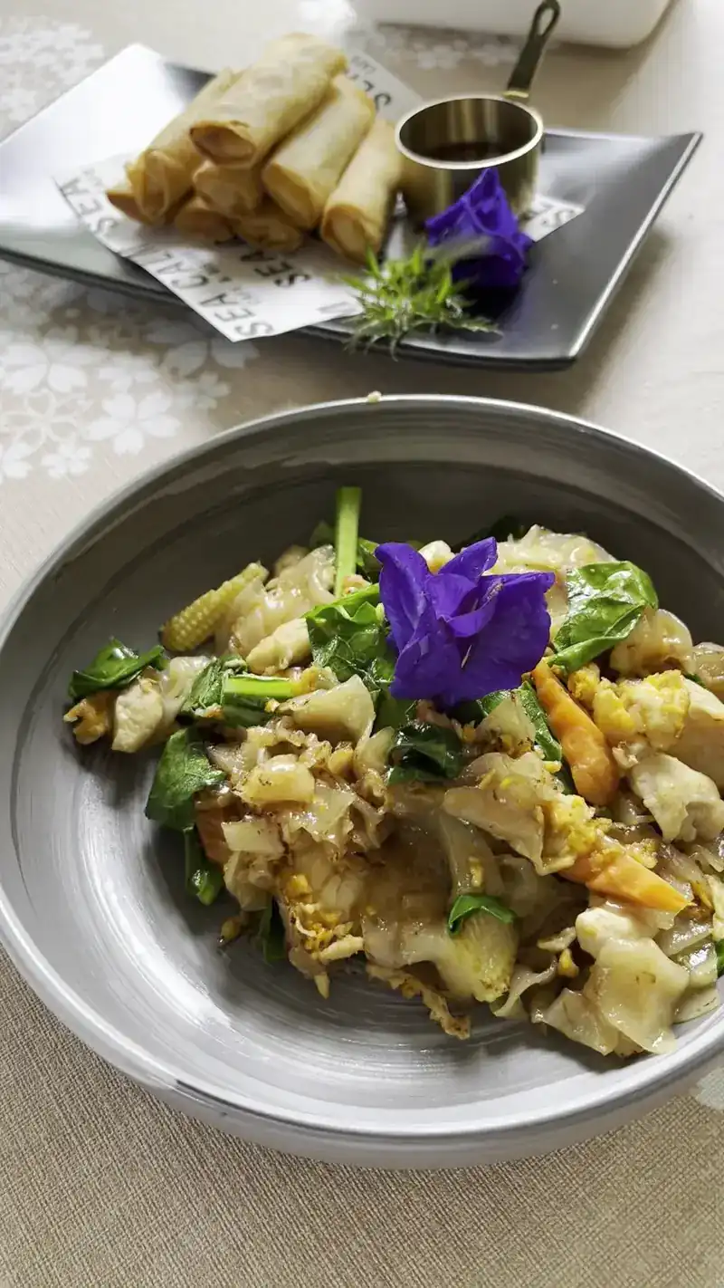 Stir-fried wide noodles with greens, and spring rolls on the side