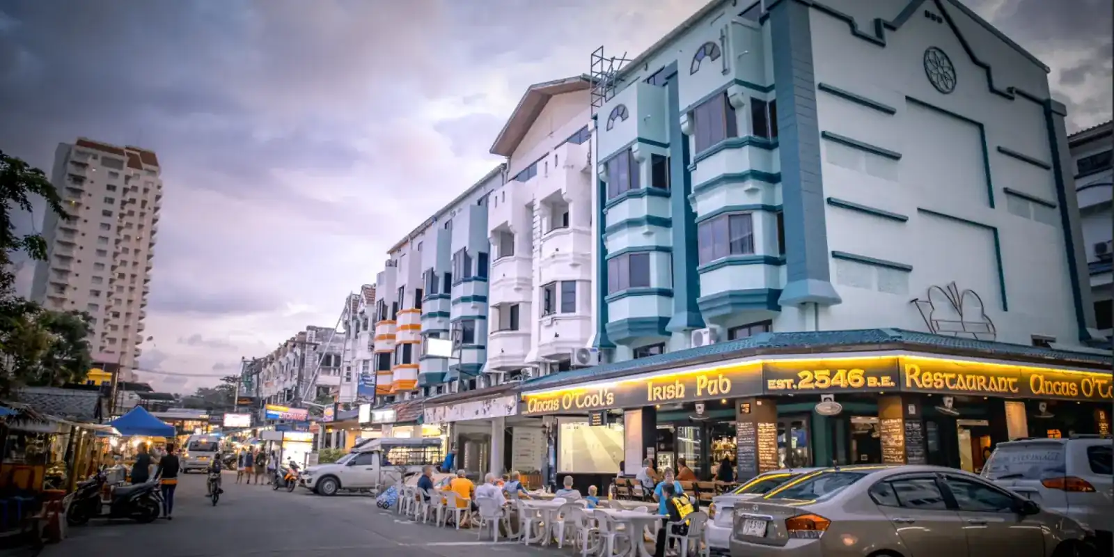 Angus O'Tool's at dusk: the gold-lettered sign along the corner of a teal and white building, with open-air tables on the street in Karon