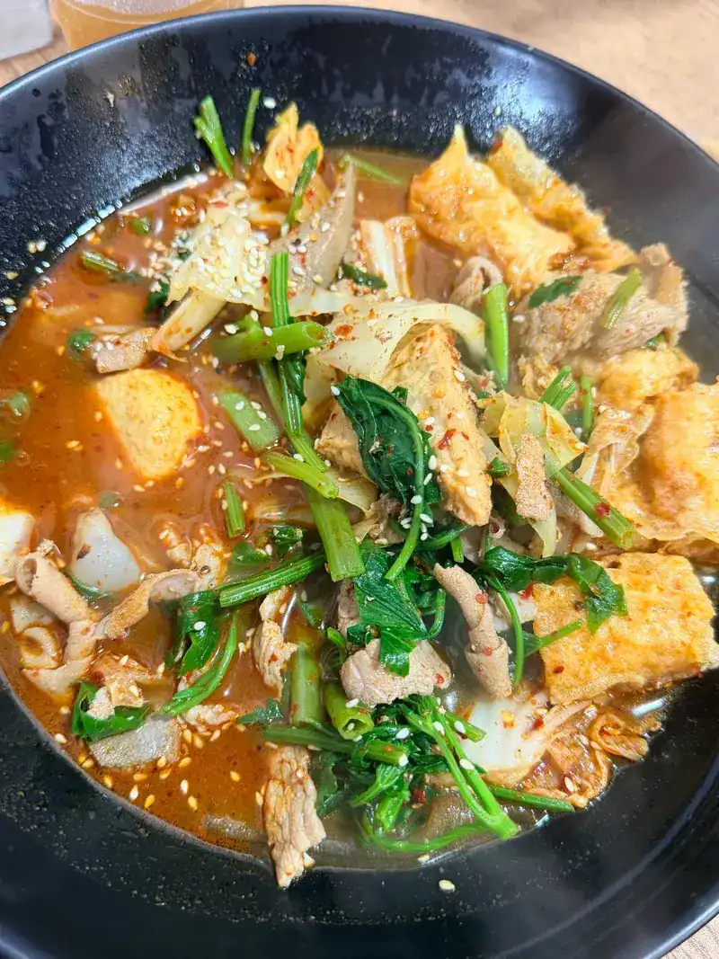 A bowl of tofu, greens and sliced pork in mala soup, topped with sesame