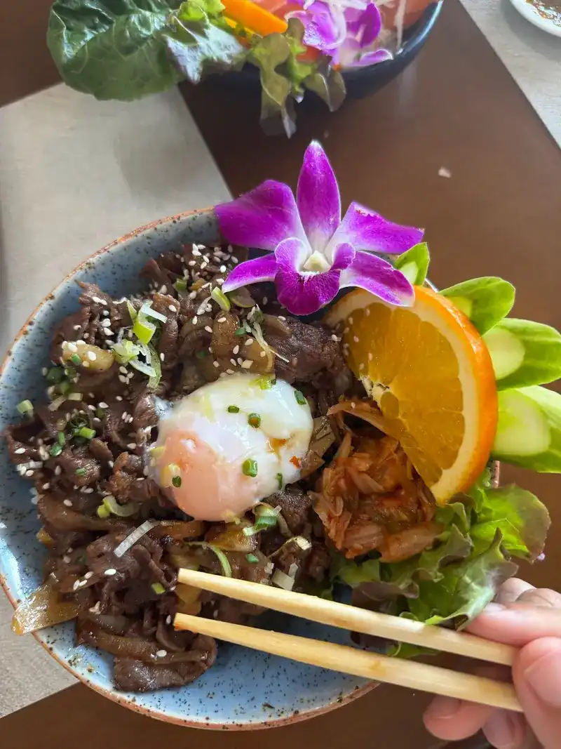 Australian beef rice bowl with an onsen egg, orange and an orchid