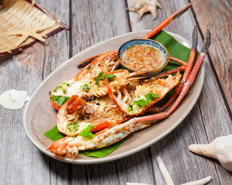 Prawns split in half and topped with herbs on a long plate, with a bowl of dipping sauce