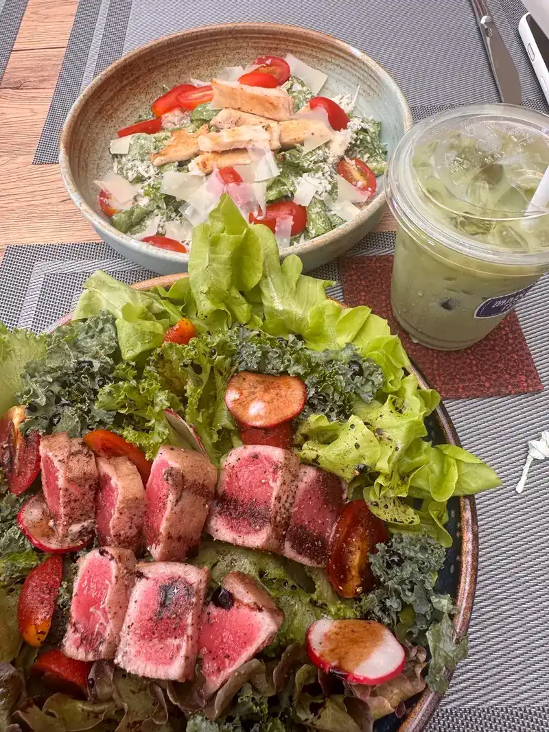 Seared tuna on salad leaves with cherry tomatoes and radish, a second salad and an iced green drink behind