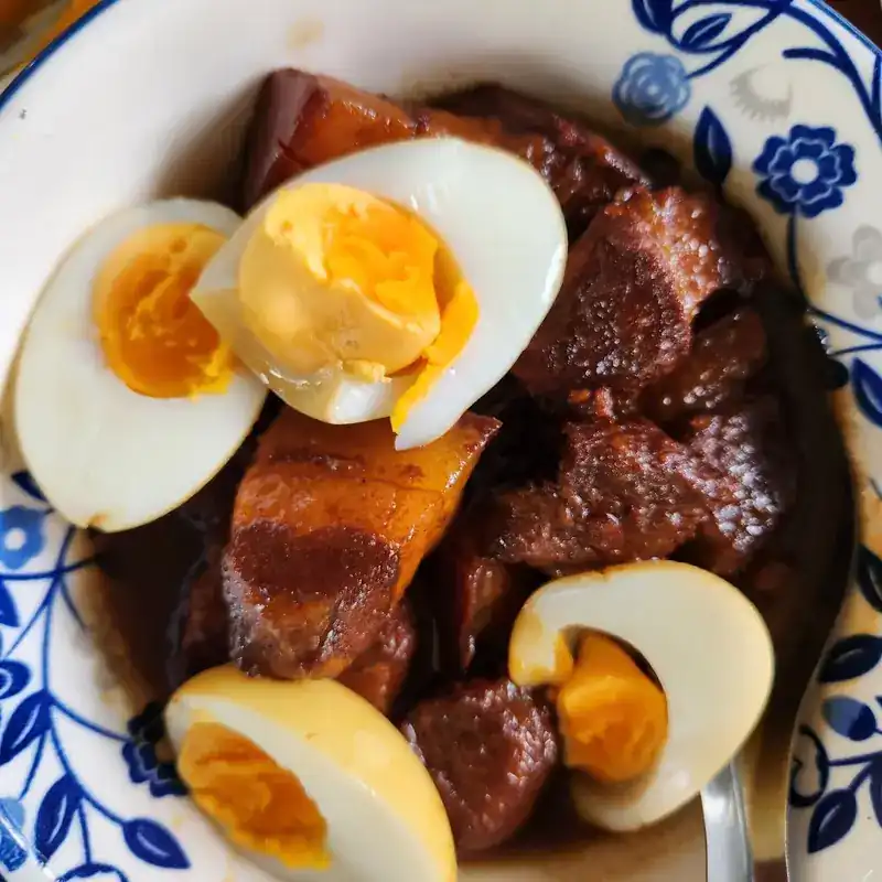 Dark braised pork belly with halved boiled eggs in a blue and white bowl