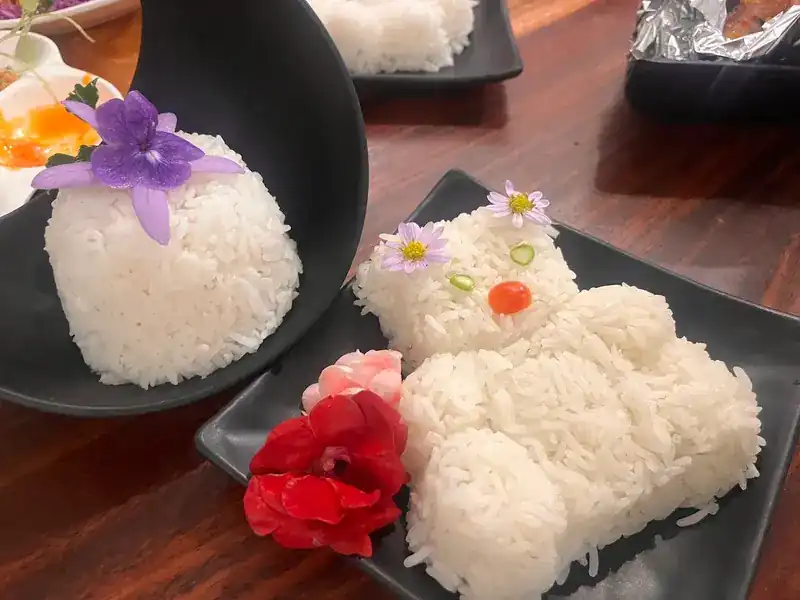 Steamed rice shaped as a teddy bear on a black plate, with flowers