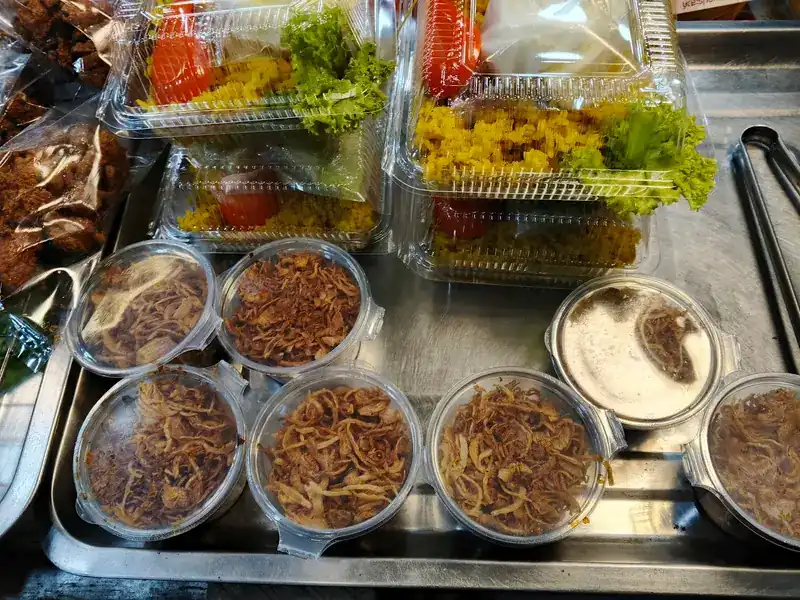 Boxes of khao mok with tomato and lettuce, and tubs of fried shallots