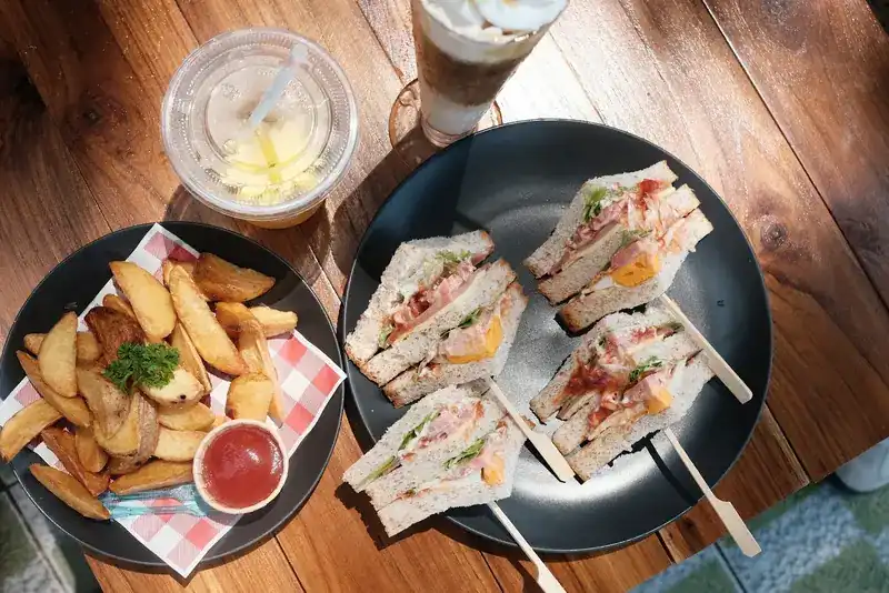 Club sandwiches, potato wedges and iced drinks on a wooden table / คลับแซนด์วิช มันฝรั่งทอด และเครื่องดื่มเย็นบนโต๊ะไม้