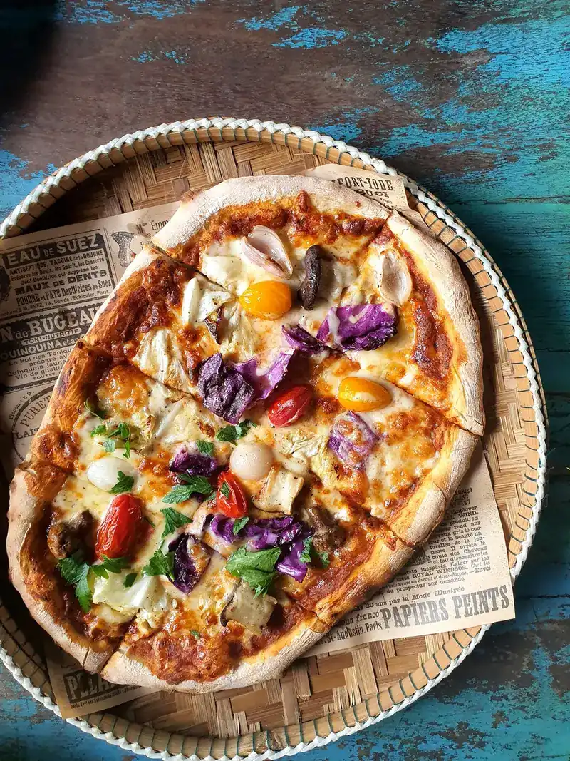A pizza with tomatoes, purple cabbage and herbs on a woven bamboo tray