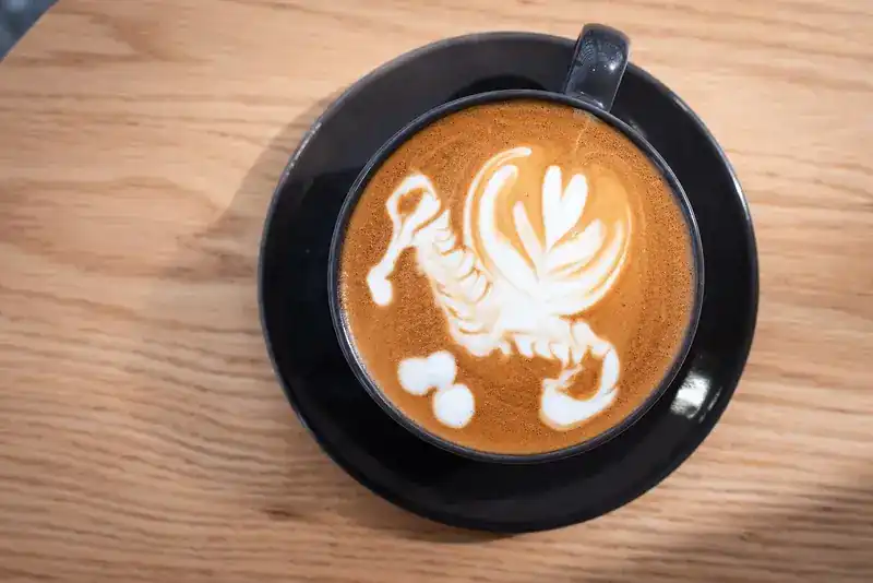Latte art in a black cup on an oak table